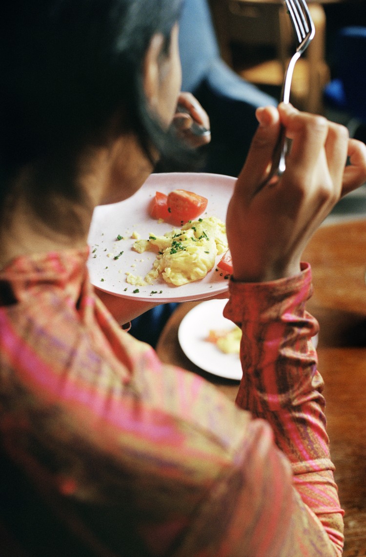 A woman in a pink shirt pauses between bites of JUST Egg on a plate with some tomatoes.