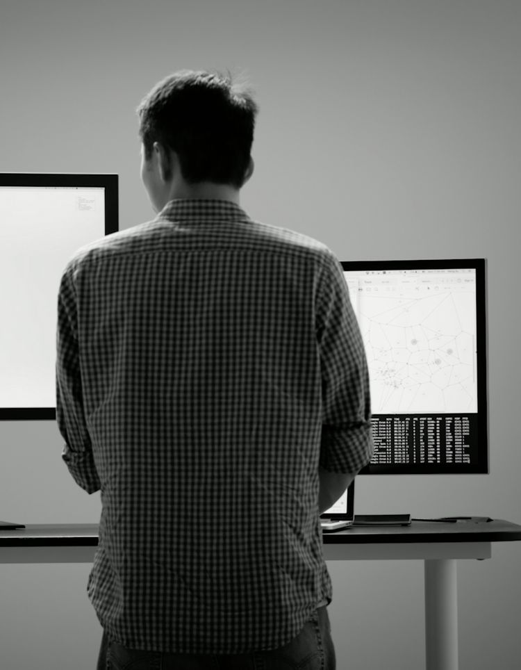 A person at a standing desk looking at two computer monitors 